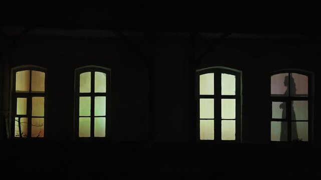 The mystical shadow of a woman's figure in the windows of the old. People Silhouettes in House Windows at Night