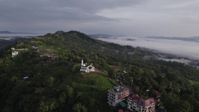 Wide drone view of a white mosque on a green mountain ridge in Sajek Valley