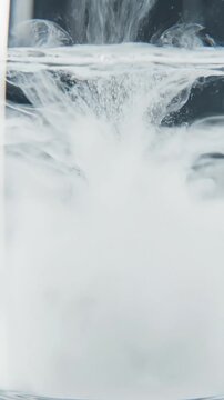White probiotic powder pouring into a glass of clear water creating a healthy cloudy suspension