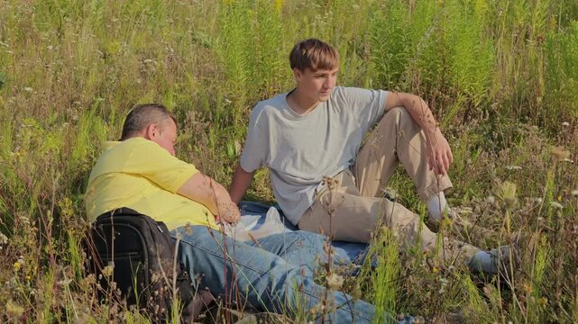 Loving father enjoys picnic. Young son eats fruits. They sit in forest. Green trees surround them. Sunny morning looks beautiful.