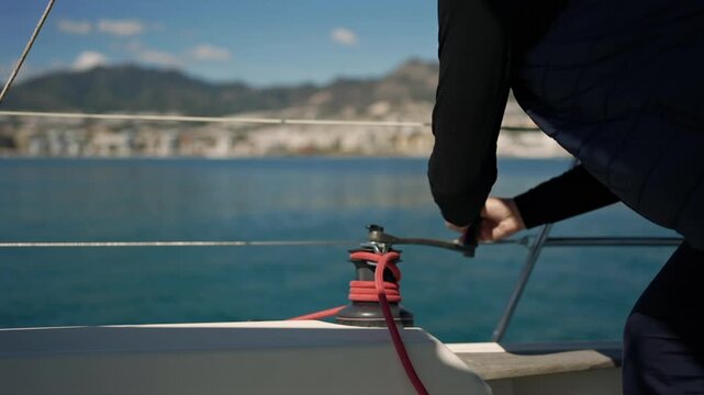 Sailor hoisting sails using a winch handle on a yacht