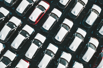 Fototapeta premium Aerial top down view of new cars parked in car parking lot. Car dealer parking lot full of new automobiles. New cars lined up for import and export business.