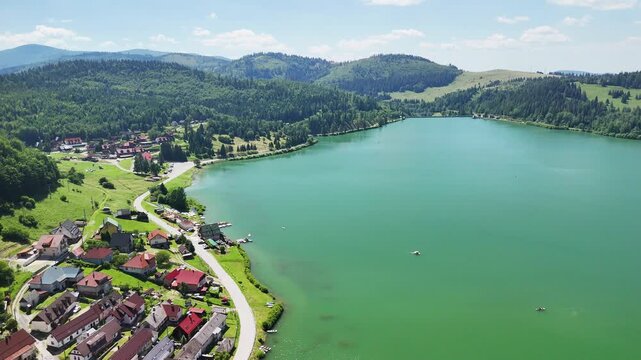 Aerial view of Palcmanska Masa lake surrounded by lush green hills and the village of Dedinky, Dedinky, Kosicky kraj, Slovakia.