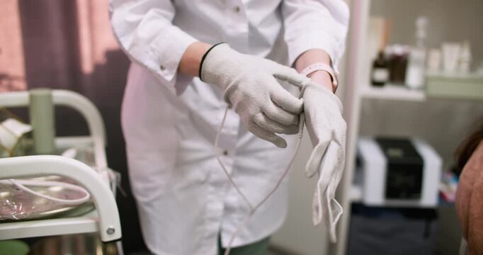 Electrotherapy gloves using. Esthetician occupation. Unrecognizable woman using microcurrent device for beauty skin treatment at modern workplace.