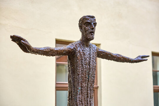 Bronze sculpture of elderly male with outstretched arms against neutral background. March 21, 2026, Telc, Czech Republic