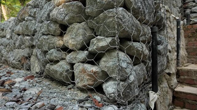 Close-up of a gabion retaining wall filled with natural stones and enclosed in steel wire mesh, showcasing durable engineering for slope stabilization and landscape construction.