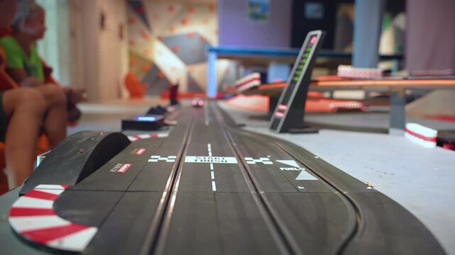 Children playing with tabletop track for cars at indoor entertainment venue. Kids enjoy slot car racing game with electronic starting lights and curved track sections in colorful playroom setting.