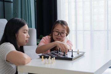 Fototapeta premium Two Asian girl playing chess board game together in living room