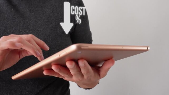 Person holds tablet with arrow pointing down labeled 'COST %'. Hands focus on device showing financial concept. Image suits budget, savings, or cost-cutting themes. Ideal for business, finance