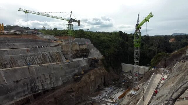 Aerial view of the PLTA Kerinci Merangin Hidro construction site with heavy machinery and concrete structures in Batang Merangin, Jambi, Indonesia.