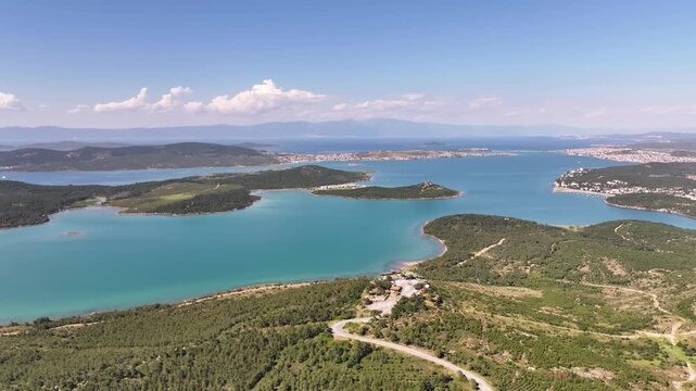 Aerial view of the Aegean coastline with turquoise waters, lush green islands, and a winding road overlooking the sea in Ayvalik, Balikesir, Turkiye.