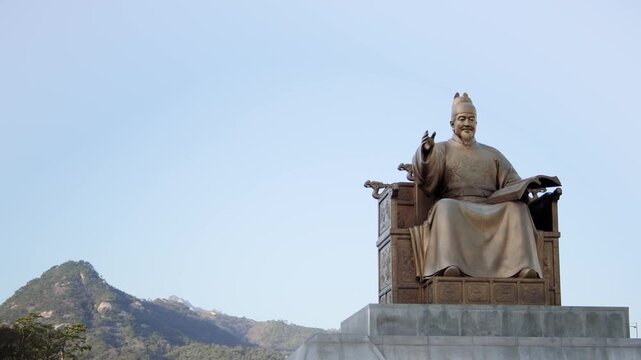 A low angle view of the bronze seated statue of King Sejong the Great against a clear blue sky at Gwanghwamun Plaza.