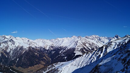 Fototapeta premium Panoramic view of snowy alpine mountain range under blue sky 