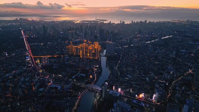 Cinematic tracking aerial shot following Pasig River in Pasig and Mandaluyong City Philippines with visible bridges, riverside roads, and Rockwell Power Plant during radiant sunset time.
