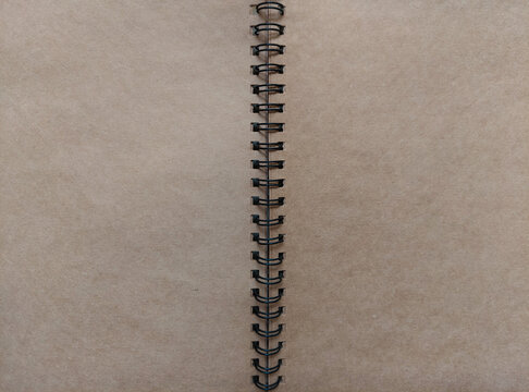 An open spiral notebook with blank, brown kraft paper pages and black metal coil binding, for stationery, copy space, background, mockup, sketchbook, journal, diary, creative design project concepts.