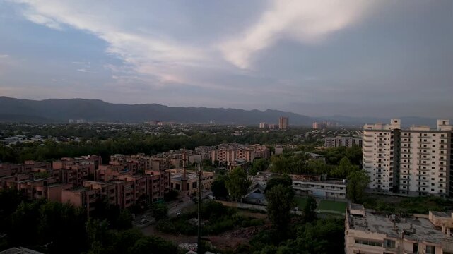 Residential districts and apartment towers extend toward the Margalla Hills beneath sweeping clouds, Islamabad, Pakistan