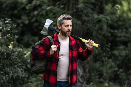 Serious lumberjack holding axe and looking away outdoors. Lumberjack worker. A lumberjack with an ax cutting trees in the forest. Man woodcutter outdoor portrait. Concept of a professional logging.