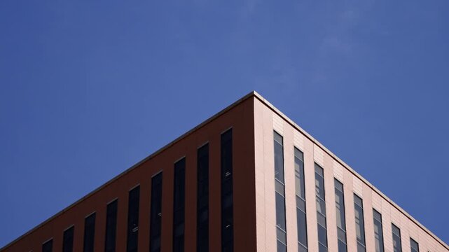 A low angle view looking up at a modern red brick building with vertical window strips against a clear blue sky.