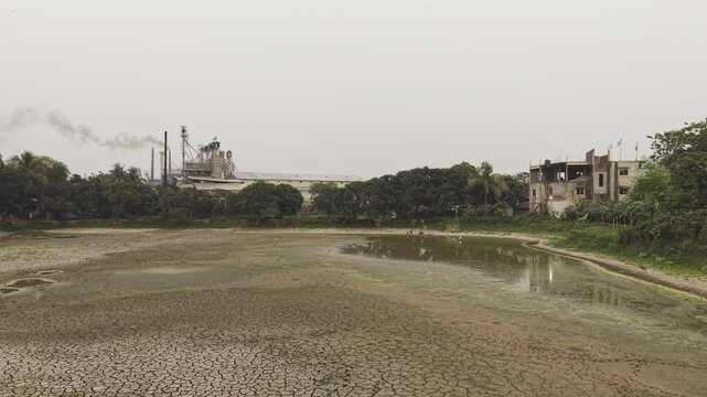 Cinematic 4K drone footage flying backwards low over a severely cracked dry lake bed in Bangladesh. The aerial view highlights drought, water scarcity, climate change, and environmental degradation.