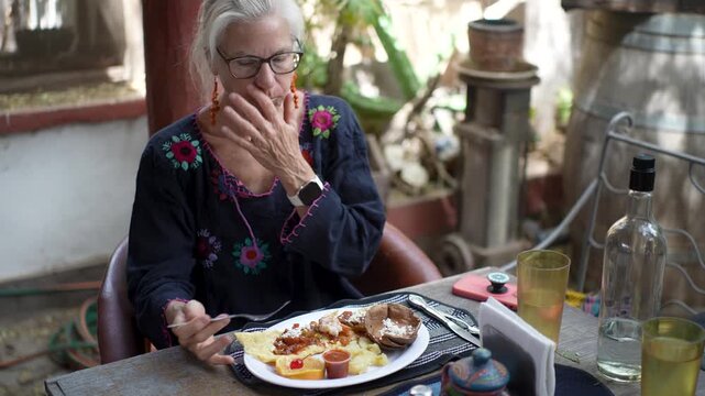 A senior woman smiles and enjoys a shrimp omelette during her meal at a restaurant in Mulege, Baja California Sur Mexico.