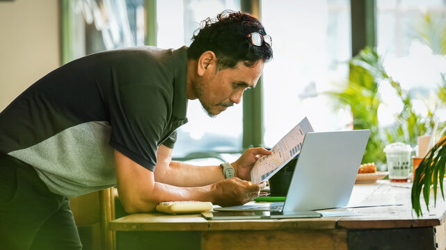 Senior businessman reviewing business reports while working on a laptop in a modern workspace. Mature entrepreneur analyzing documents