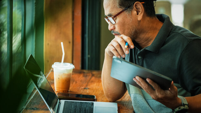 Senior Businessman Working with Laptop and Digital Tablet in Coffee Shop