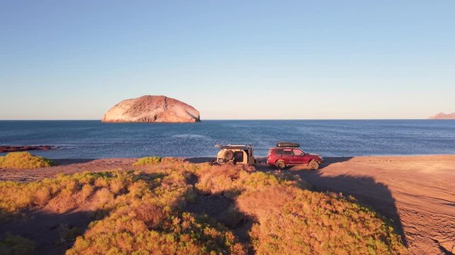 Sunset camping on the beach with an suv and a teardrop camper in Baja California, Mexico with views of the ocean and desert.