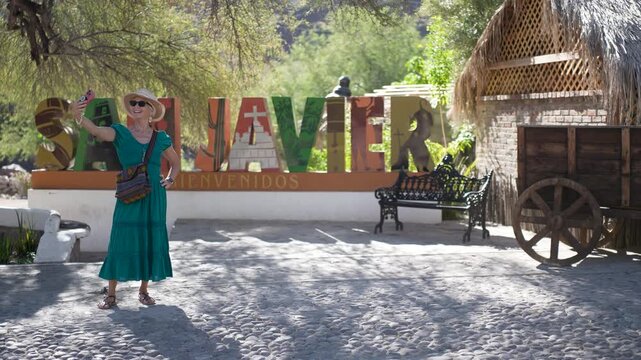Happy senior woman takes selfies in front of the San Javier sign at sunrise near Loreto in Baja California Sur, Mexico