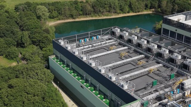Aerial view of a modern data center facility with cooling units and industrial infrastructure situated near a green forest and a small lake in London, London, United Kingdom.