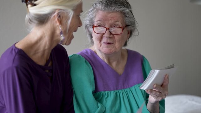 Mature daughter shares photos and stories with elderly mother during a visit at the senior care facility in the afternoon light
