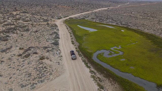 Suv pulls a teardrop camper trailer through sand while exploring a scenic overland area near Guerrero Negro Baja California Mexico.