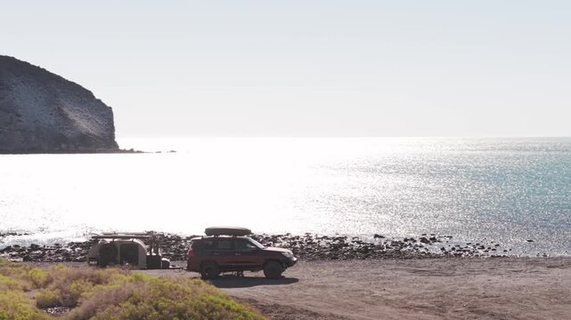 Suv and teardrop camper trailer set up on the beach at sunrise by the Sea of Cortez during an overland adventure in Baja California