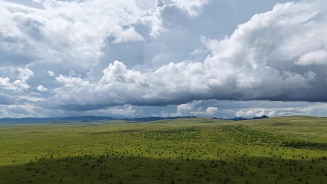 Dramatic storm clouds gathering over vast green hills and wilderness plains before heavy rain, atmospheric panoramic landscape of approaching bad weather in the valley.
