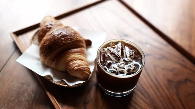 Fresh croissant served with iced coffee on a wooden table, perfect for breakfast, brunch, or a relaxing caf&eacute; break.