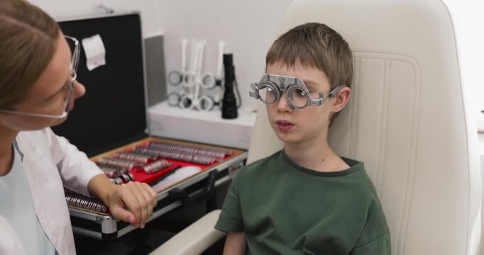Optometrist performing pediatric refraction test assessing eyesight condition of child with trial frame fitting choosing, appropriate lenses for vision correction and prescription glasses selection