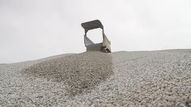 A dump truck empties a load of gravel on a high pile, illustrating the process of raw material transport crucial to construction projects and infrastructure