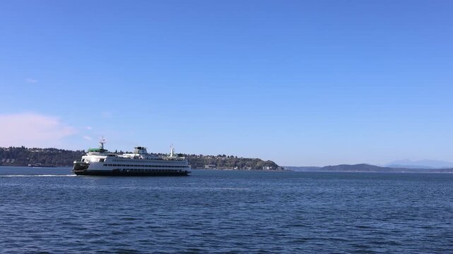 View of a ferry crossing Elliott Bay with distant hills under a clear blue sky in Seattle, Washington, United States.