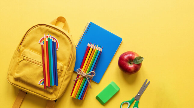 Flat lay top view of a yellow school backpack with colorful pencils notebook apple and scissors on a vibrant background for educational preparation