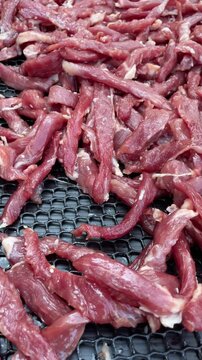 Sun-dried pork slices spread on a woven bamboo basket, a traditional Thai food preservation method.