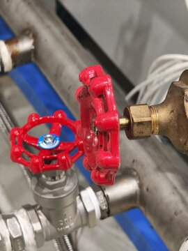 A close-up view of two red handwheel valves connected to brass and stainless steel pipes in a factory