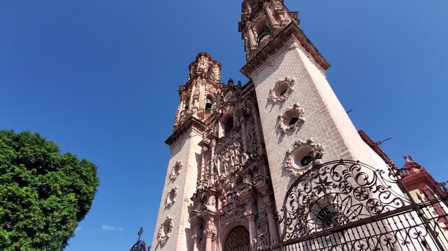 View of the ornate facade and twin bell towers of Santa Prisca de Taxco church under a clear blue sky in Taxco, Guerrero, Mexico.