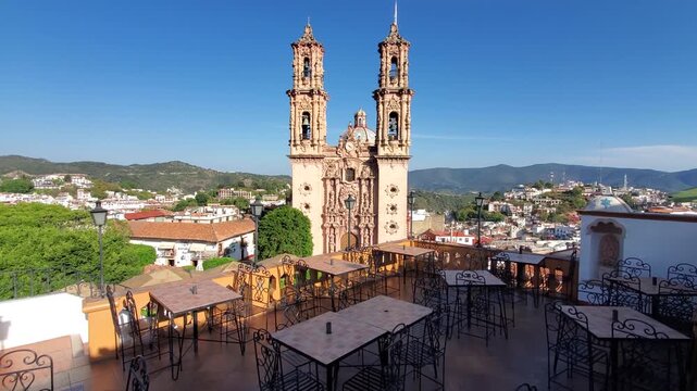 View of Santa Prisca de Taxco from a terrace with tables and chairs overlooking the historic city of Taxco, Guerrero, Mexico.