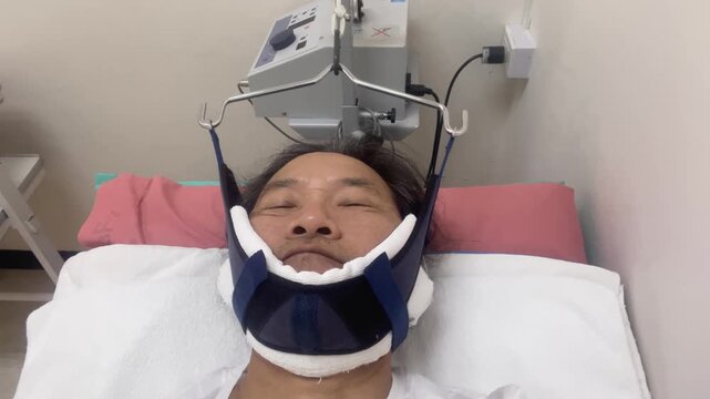 Asian man receiving cervical traction therapy with a medical device in a hospital bed. Treatment for neck pain, pinched nerve, or cervical spine herniated disc.