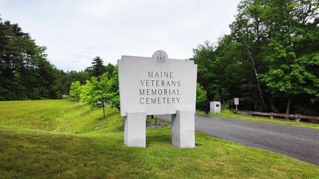 Maine Veterans Memorial Cemetery sign above a mowed lawn slope in Augusta