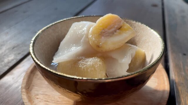 Banana in coconut milk or Kluai Buat Chi. Traditional Thai sweet dessert served in a ceramic bowl on a wooden table.