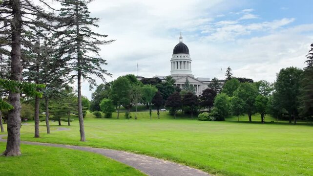 Maine State House on an overcast day with a paved footpath curving across green lawns