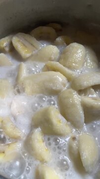 Banana in coconut milk or Kluai Buat Chi. Traditional Thai sweet dessert served in a ceramic bowl on a wooden table.