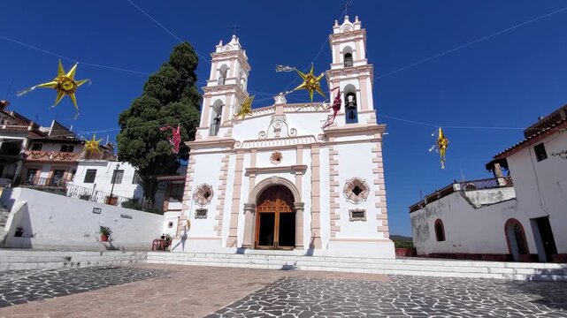 View of the historic church in Taxco with its white facade and twin towers, decorated with hanging stars in the square, Taxco, Guerrero, Mexico.
