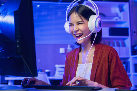 Young Asian woman playing online computer game with headset at home, esports and live streaming concept.