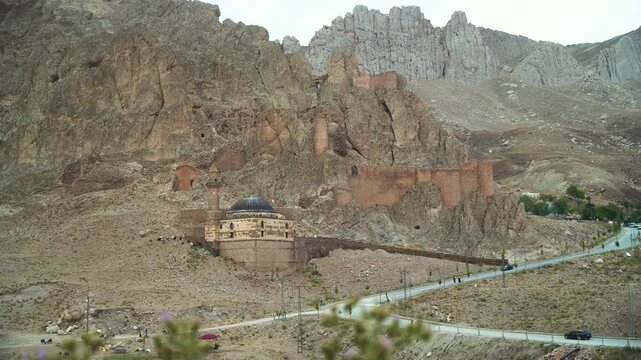 View of Ishak Pasha Palace with its historic stone walls and mosque dome set against rugged mountain cliffs in Turkey.